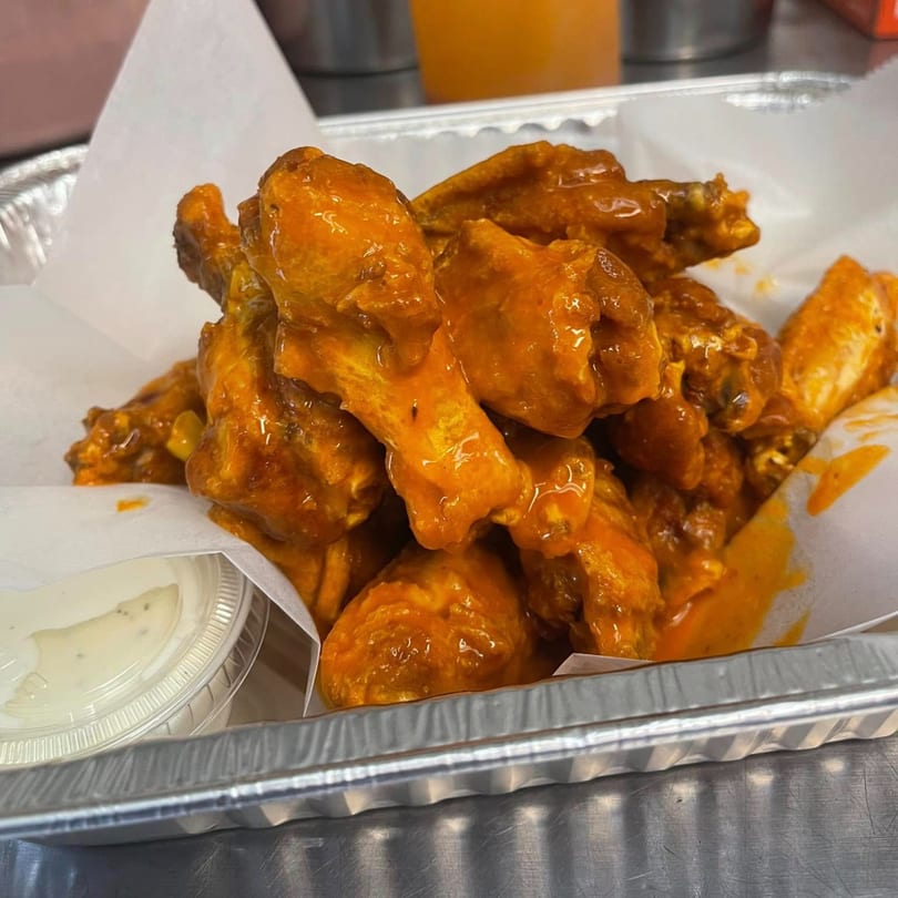 A foil container filled with buffalo wings and a side of ranch dressing from Hampton Hill Pizza.
