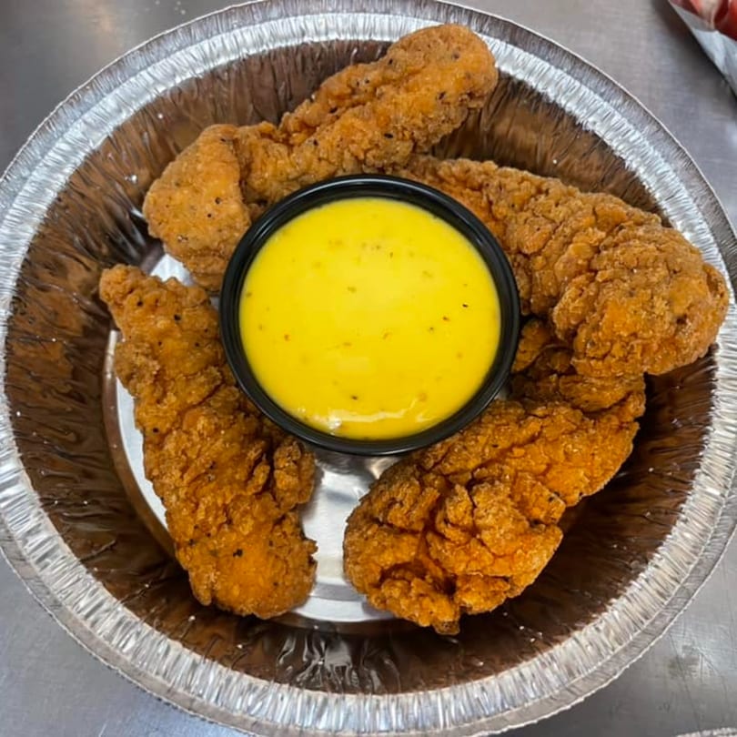 Crispy chicken tenders with a side of bright yellow dipping sauce in a foil container.