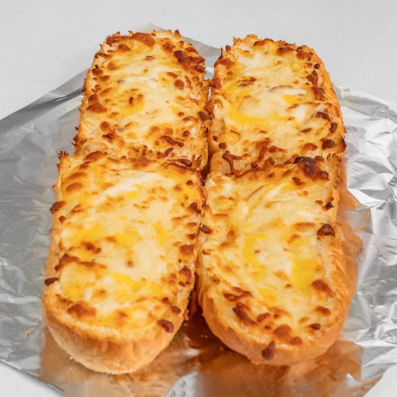 Four golden-brown Hampton Hill Pizza cheesy breadsticks, topped with melted cheese, on aluminum foil.